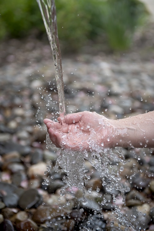 Closeup of a hand reaching out as a stream of water comes from a above to splash of it.