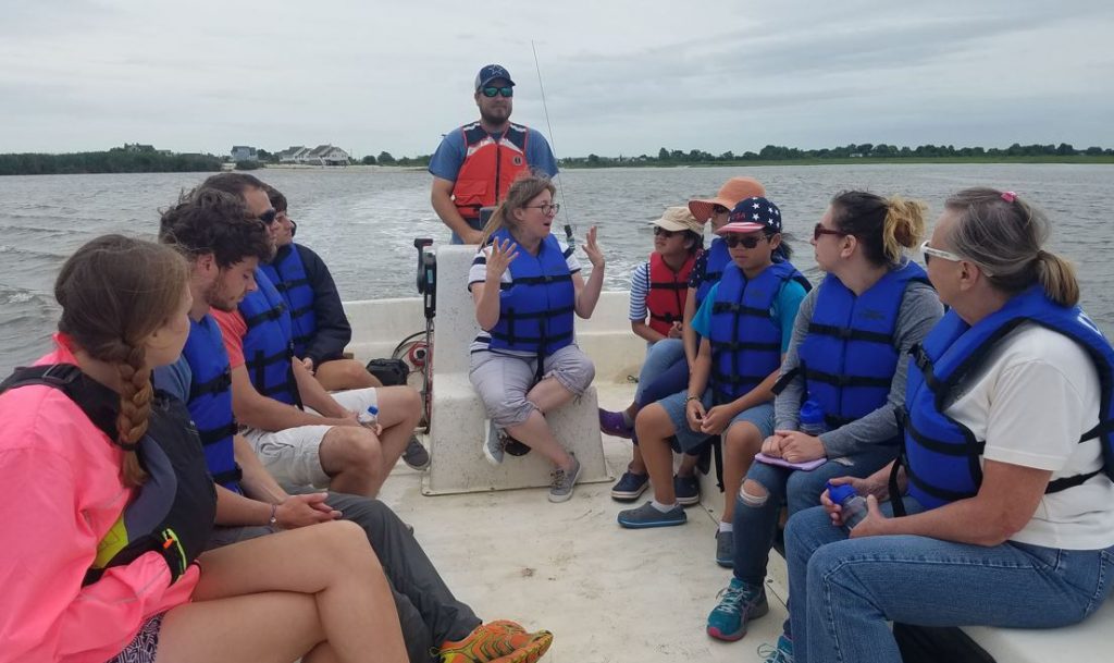 A group listens to a nature reserve staff person speak while riding in an open boat.